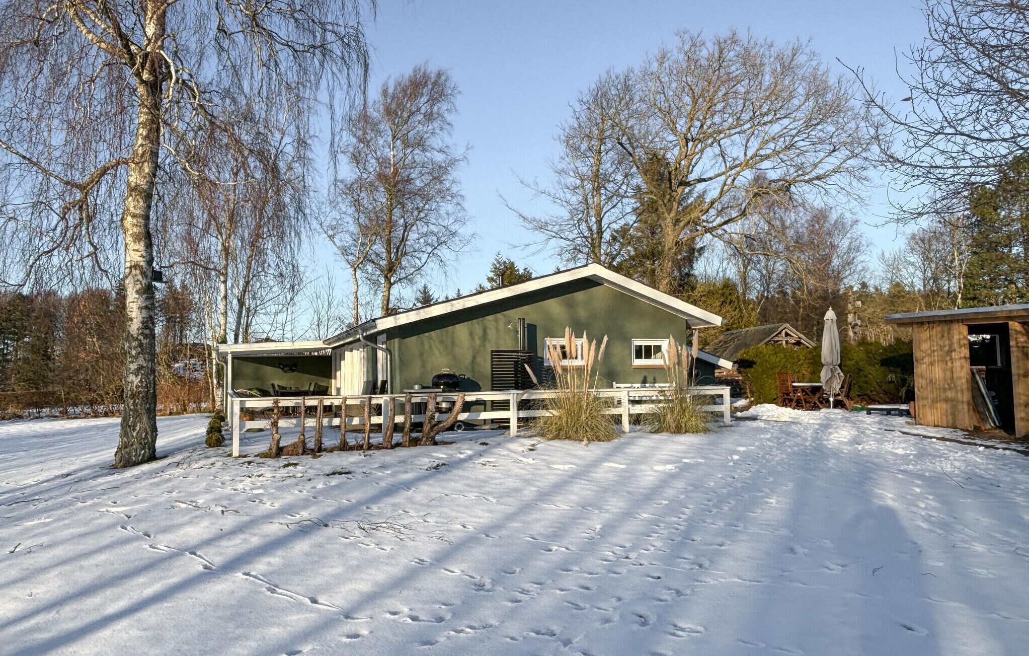 Un bâtiment d’un seul étage, à l’extérieur vert, avec un porche blanc et une clôture en bois.