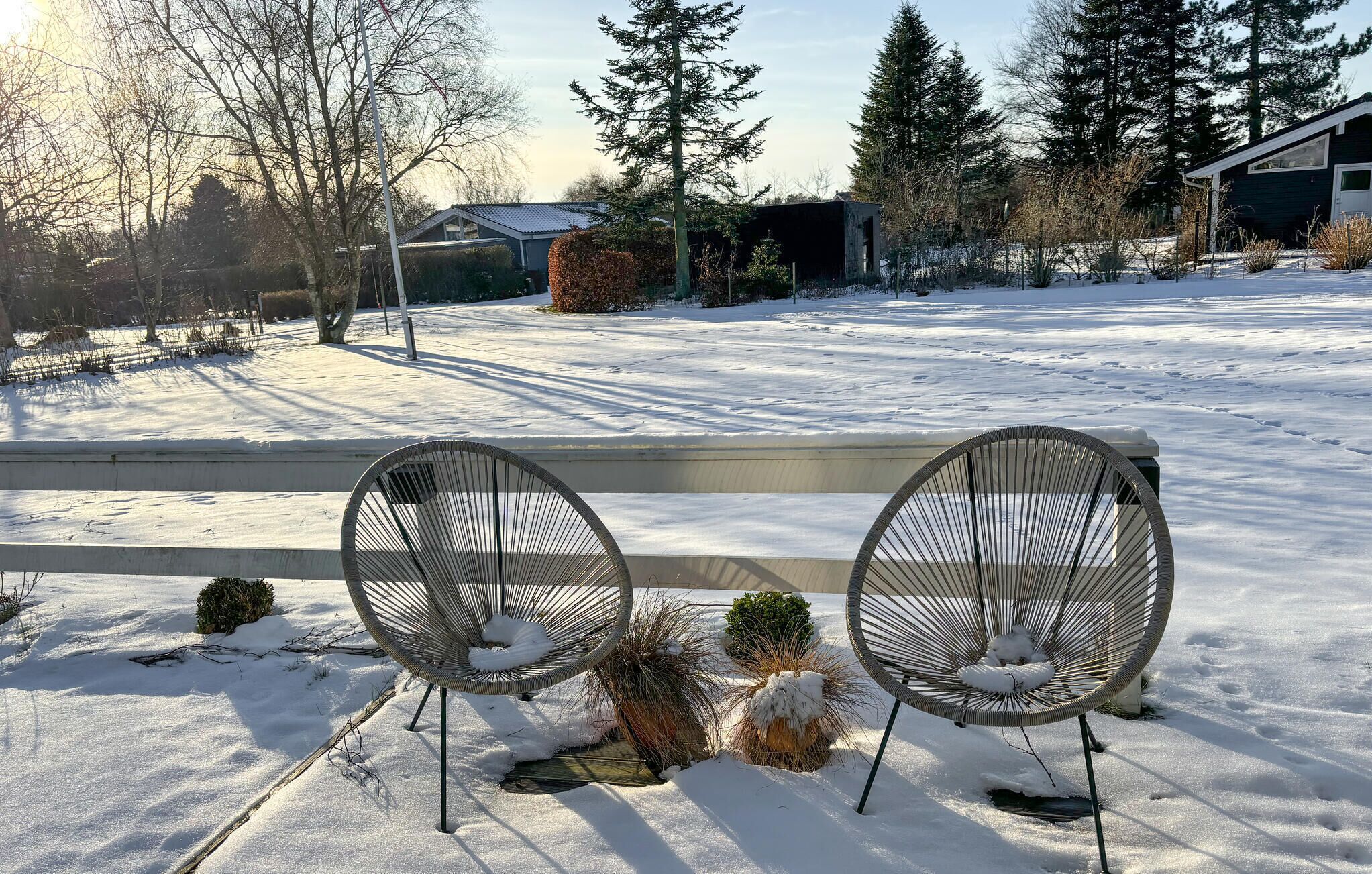 Un banc avec deux chaises, situé dans un espace extérieur enneigé, avec des arbres et un bâtiment en arrière-plan.