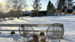 A bench with two chairs in a snowy outdoor area with trees and a building in the background. - 3 bedroom awesome home in Farsø (Farsø)