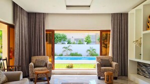 Sala moderna com duas poltronas estampadas, um sofá, uma mesa de centro e vista para uma piscina e jardim.