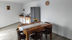 Een eetgedeelte met een houten tafel en stoelen, een klok aan de muur en een keuken op de achtergrond.