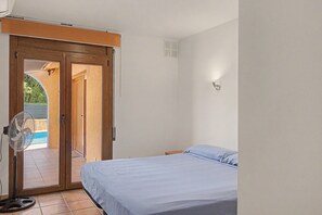 Une chambre à coucher avec un lit, un ventilateur et une porte coulissante donnant sur un espace extérieur.