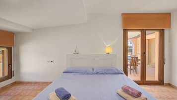 Un dormitorio con cama, dos toallas, una mesita de noche, una lámpara y vistas a un espacio exterior con mesa y sillas.