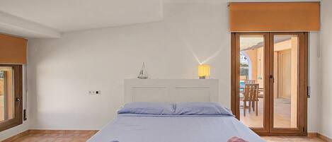 Un dormitorio con cama, dos toallas, una mesita de noche, una lámpara y vistas a un espacio exterior con mesa y sillas.
