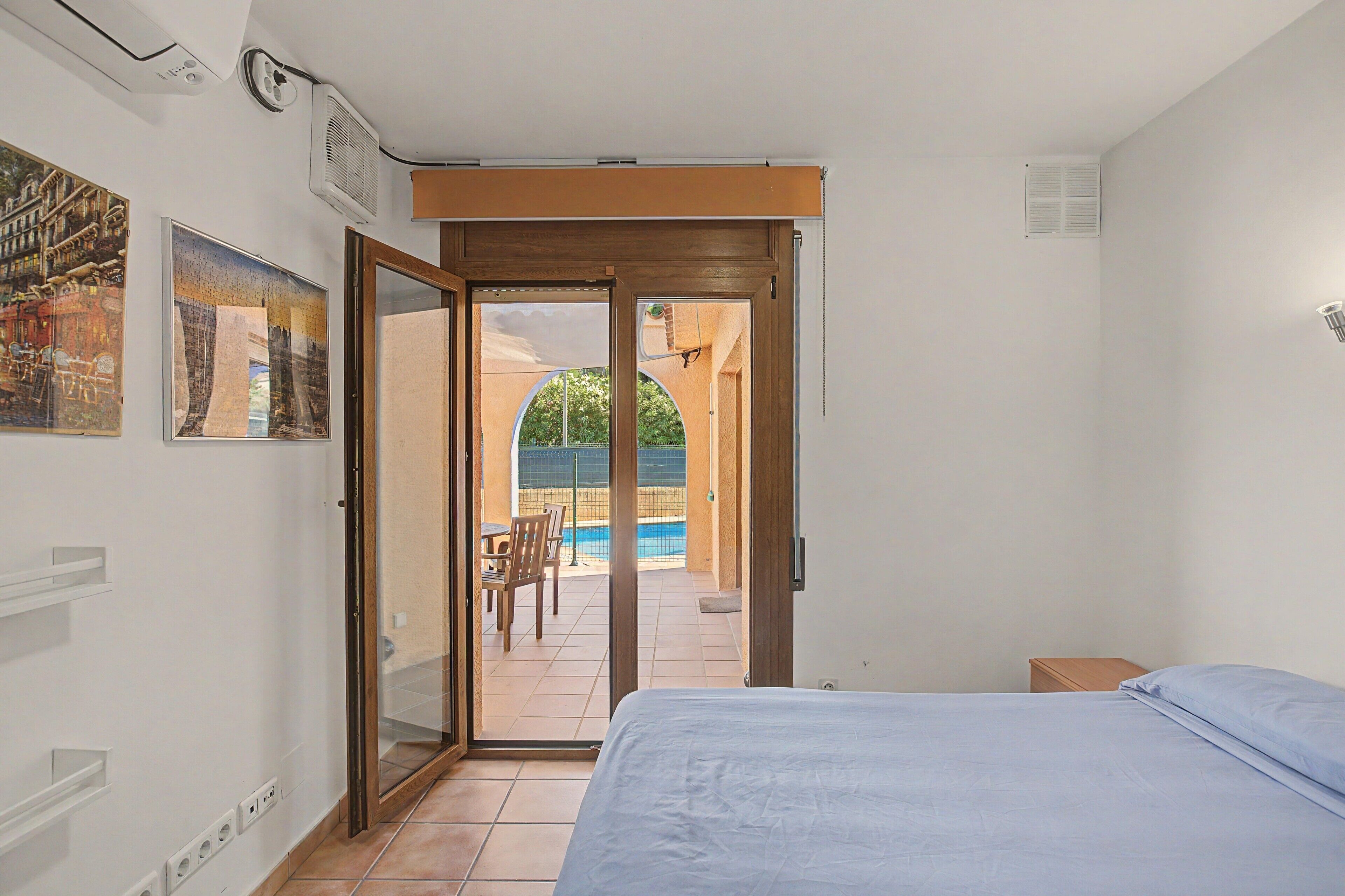 Une chambre avec un lit, une porte-fenêtre coulissante donnant sur une terrasse avec une piscine et des chaises.