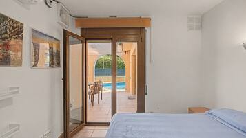 Une chambre avec un lit, une porte-fenêtre coulissante donnant sur une terrasse avec une piscine et des chaises.