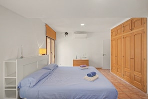 A bedroom with a bed, a wardrobe, a bedside table, a lamp, and an air conditioning unit.
