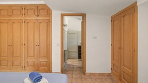 A bedroom with a bed, wooden wardrobe, and a bathroom visible through an open door.