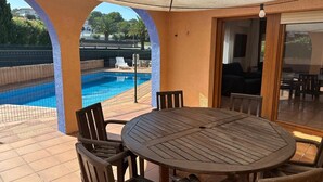 An outdoor patio with a round wooden table and chairs, a swimming pool, and a covered area with a view of the surrounding landscape. - Villa Antic Plankton - Masos de Pals – Free Parking, Beach, Wifi, Holidays (Els Masos de Pals)