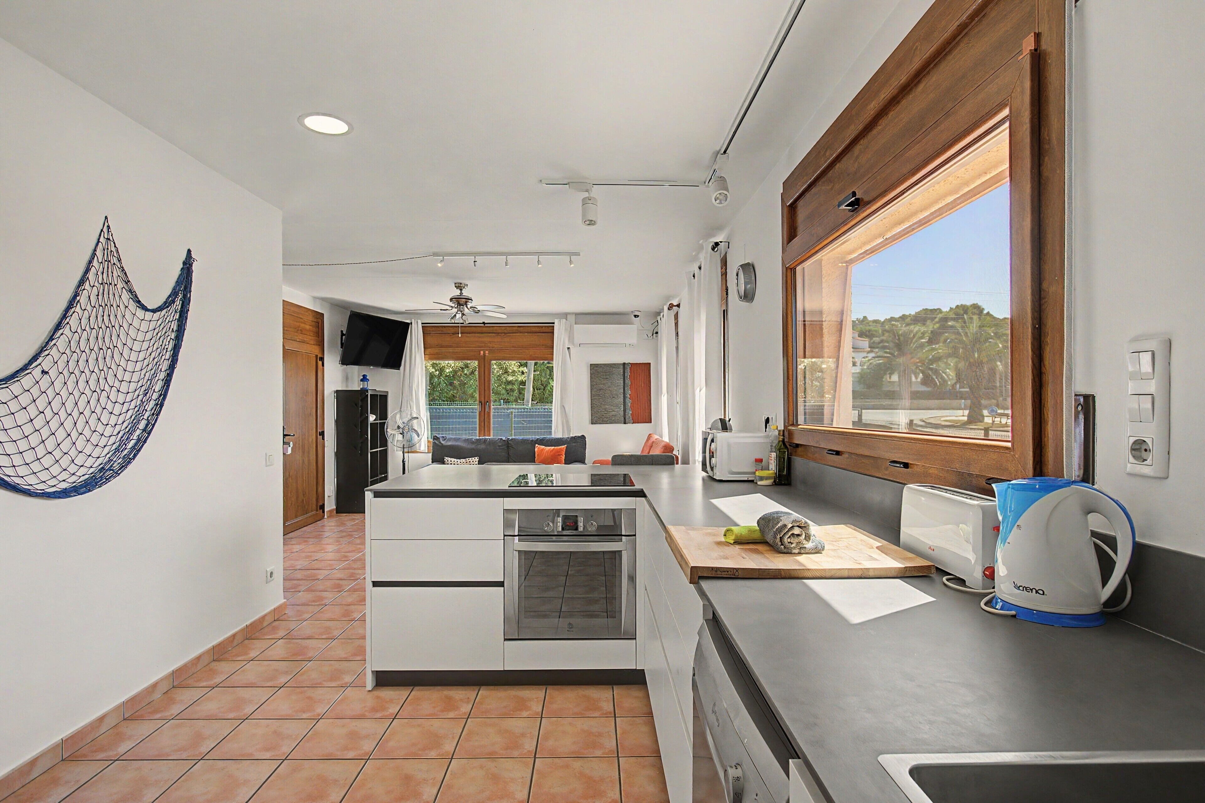 A modern kitchen with a built-in oven, a coffee maker, and a window with a view of greenery.