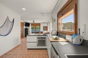 A modern kitchen with a built-in oven, a coffee maker, and a window with a view of greenery.