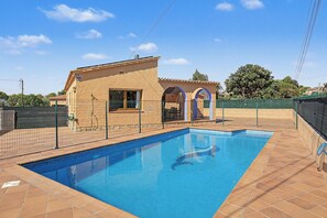 A swimming pool with a tiled deck, a fenced area, and a building with a tiled roof and arched windows.