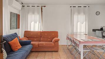 Una sala de estar con sofá, una mesa de comedor con sillas y una zona de cocina.