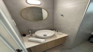 Ein modernes Badezimmer mit einem runden Spiegel, einem weißen Waschbecken und einem Handtuch auf der Ablagefläche.