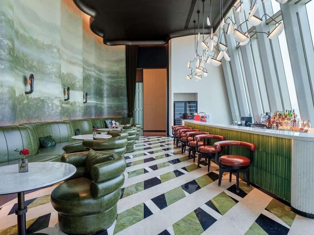 Un espace bar doté d’un coin salon avec des sièges rembourrés de couleur verte, d’un sol à motifs et d’un comptoir avec des tabourets.