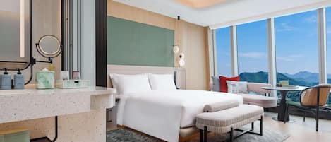 A modern hotel room with a large bed, a sitting area with a view, and a bathroom with a vanity and mirror.