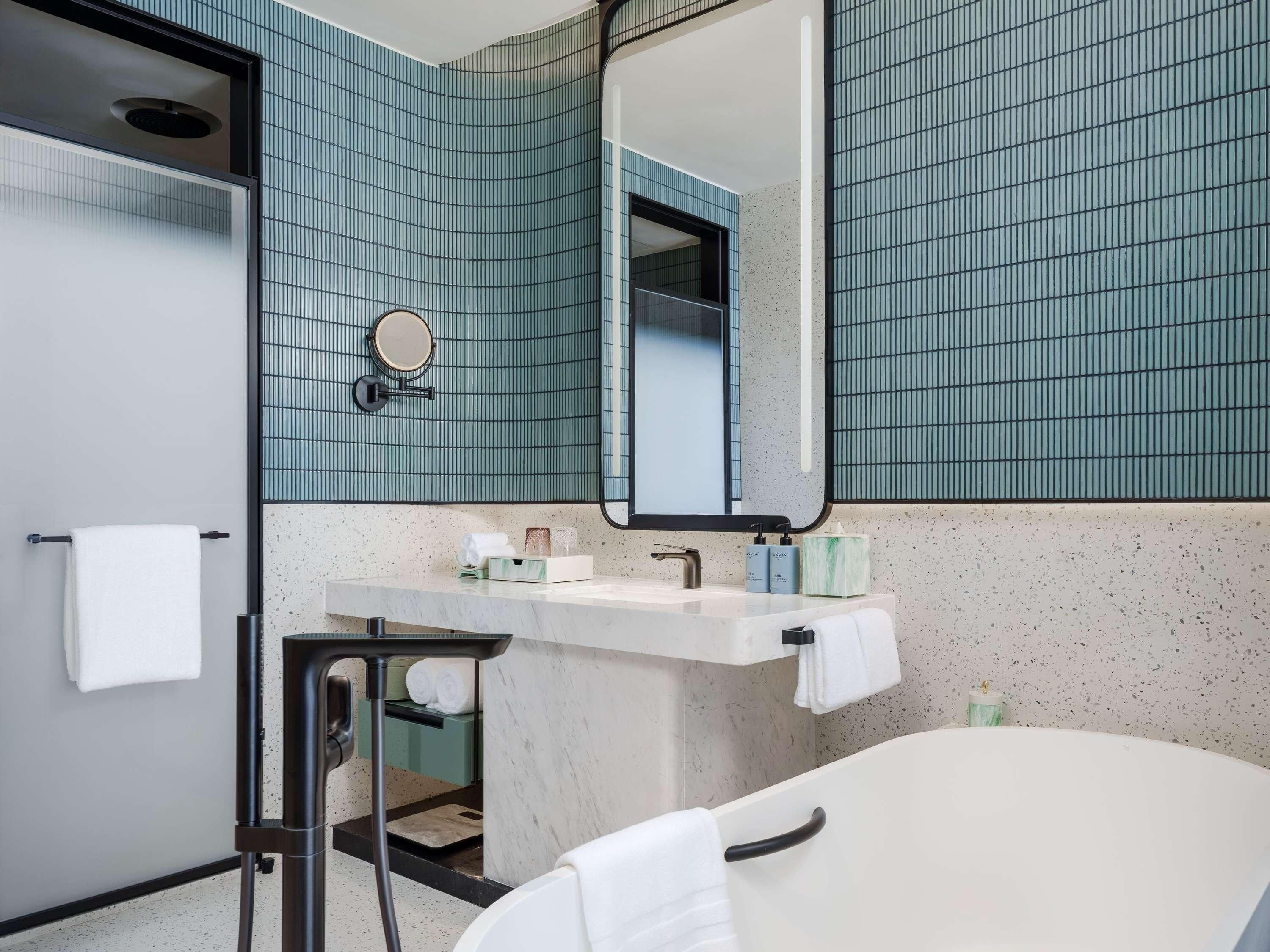 A bathroom with a white bathtub, a sink with toiletries, a mirror, and a towel rack.