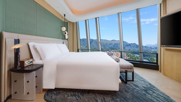 Una habitación de hotel moderna con una cama grande, mesita de noche, lámpara y televisor.