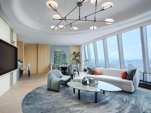 A modern living room with a sofa, chairs, a coffee table, and a large window offering a city view.