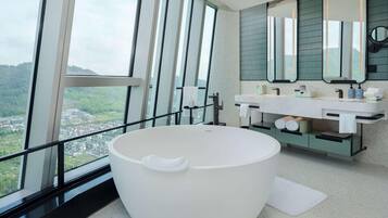 A modern bathroom with a large bathtub, a vanity with a mirror, and a view of a green landscape through large windows.