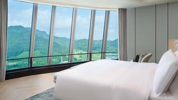 A hotel room with a large bed, a view of green hills, and a modern design.