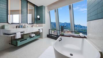Ein modernes Badezimmer mit einer freistehenden Badewanne, einem großen Spiegel und Bergblick durch hohe Fenster.
