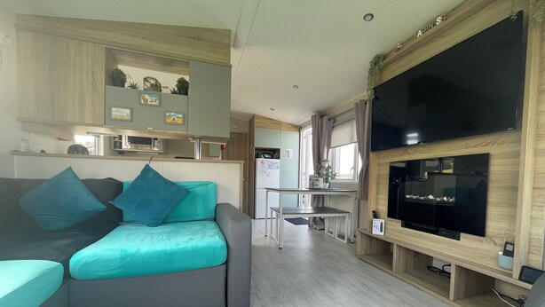 Un espacio habitable compacto con sofá, televisor, zona de cocina y mesa de comedor.
