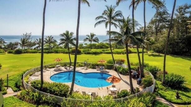 A swimming pool surrounded by palm trees and a view of the ocean. - Oceanfront condo in Kapa’a, newly remodeled and ready for you to enjoy Kauai (Lihue)