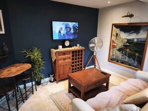 Un soggiorno con televisore, mobili in legno, una ventola e un quadro appeso al muro.