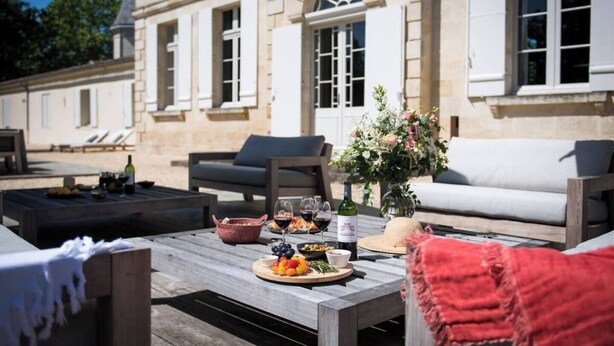 Un espace extérieur aménagé avec une table dressée pour un repas, une bouteille de vin et un vase de fleurs.
