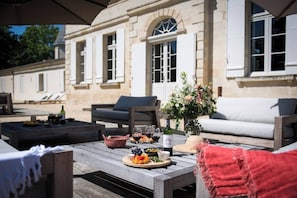 Un espace extérieur aménagé avec une table dressée pour un repas, une bouteille de vin et un vase de fleurs.
