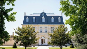 Un grand bâtiment imposant, doté d’une façade symétrique, d’une entrée centrale et d’un jardin à la française, avec des haies et des arbres taillés.