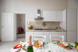 A modern kitchen with white cabinets, a stainless steel range hood, and a dining area with a table set for two. - Elegant detached house in the city center (Avola)