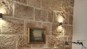 A room with a stone wall, a wooden bench, a bed with a floral bedspread, and a painting. - Elegant detached house in the city center (Avola)