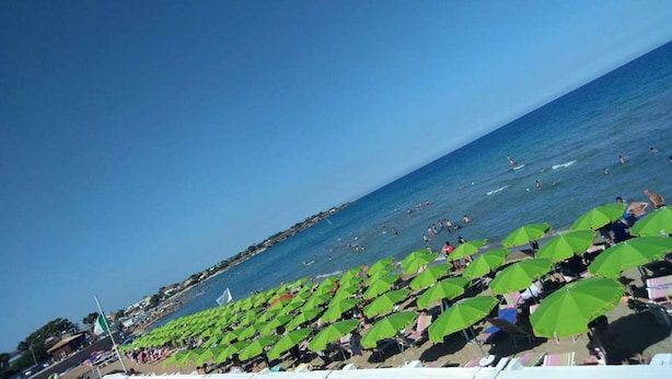 A beach with rows of green umbrellas and people swimming in the water. - Elegant detached house in the city center (Avola)