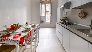 A bright kitchen with white cabinets, a stainless steel countertop, and a window with a view of buildings. - Elegant detached house in the city center (Avola)