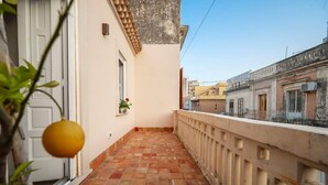 A narrow outdoor corridor with a tiled floor, a white door, and a small window with a plant. - Elegant detached house in the city center (Avola)
