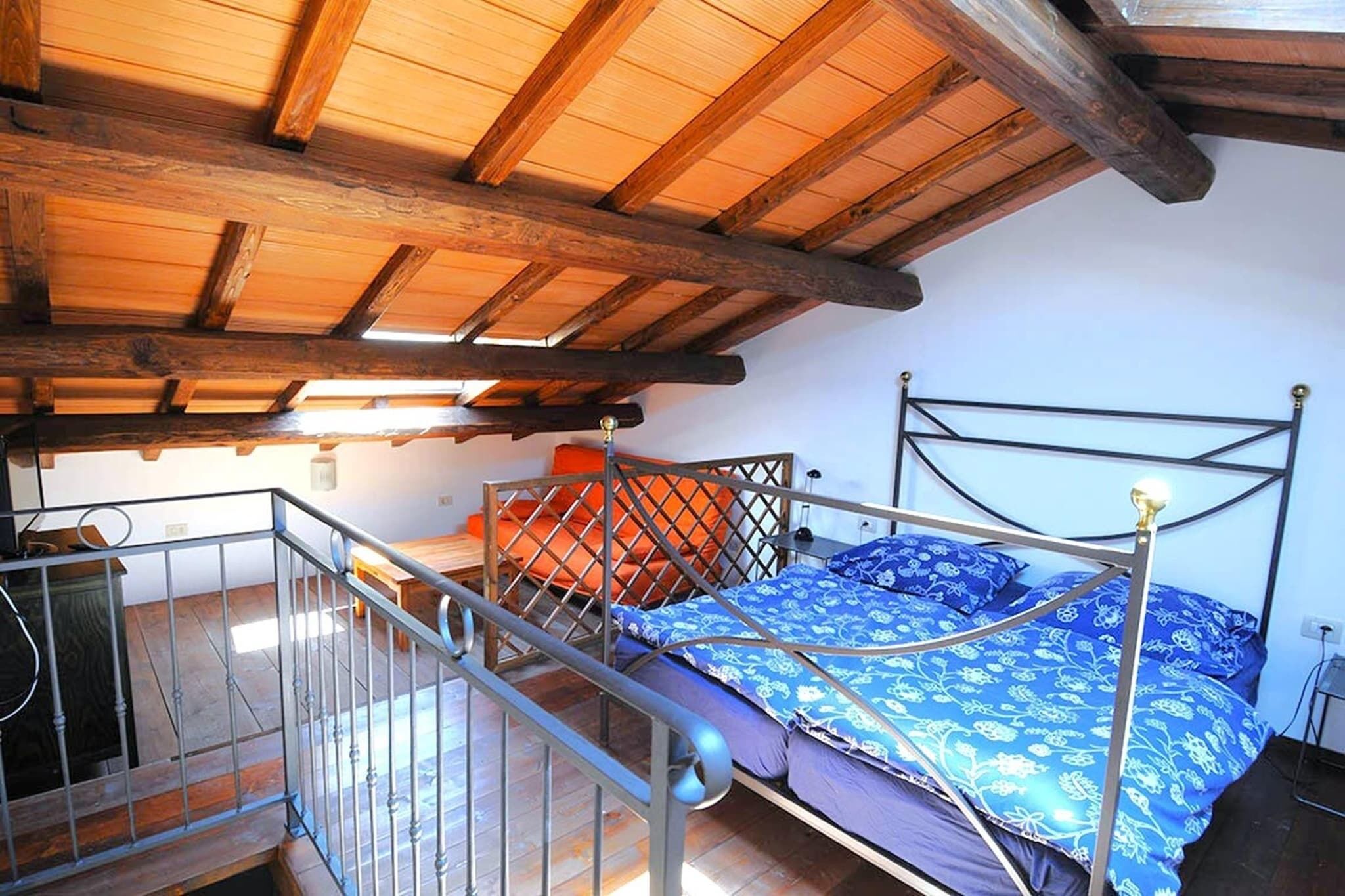 Un dormitorio con estructura de cama de metal, techo de madera y una ventana pequeña.