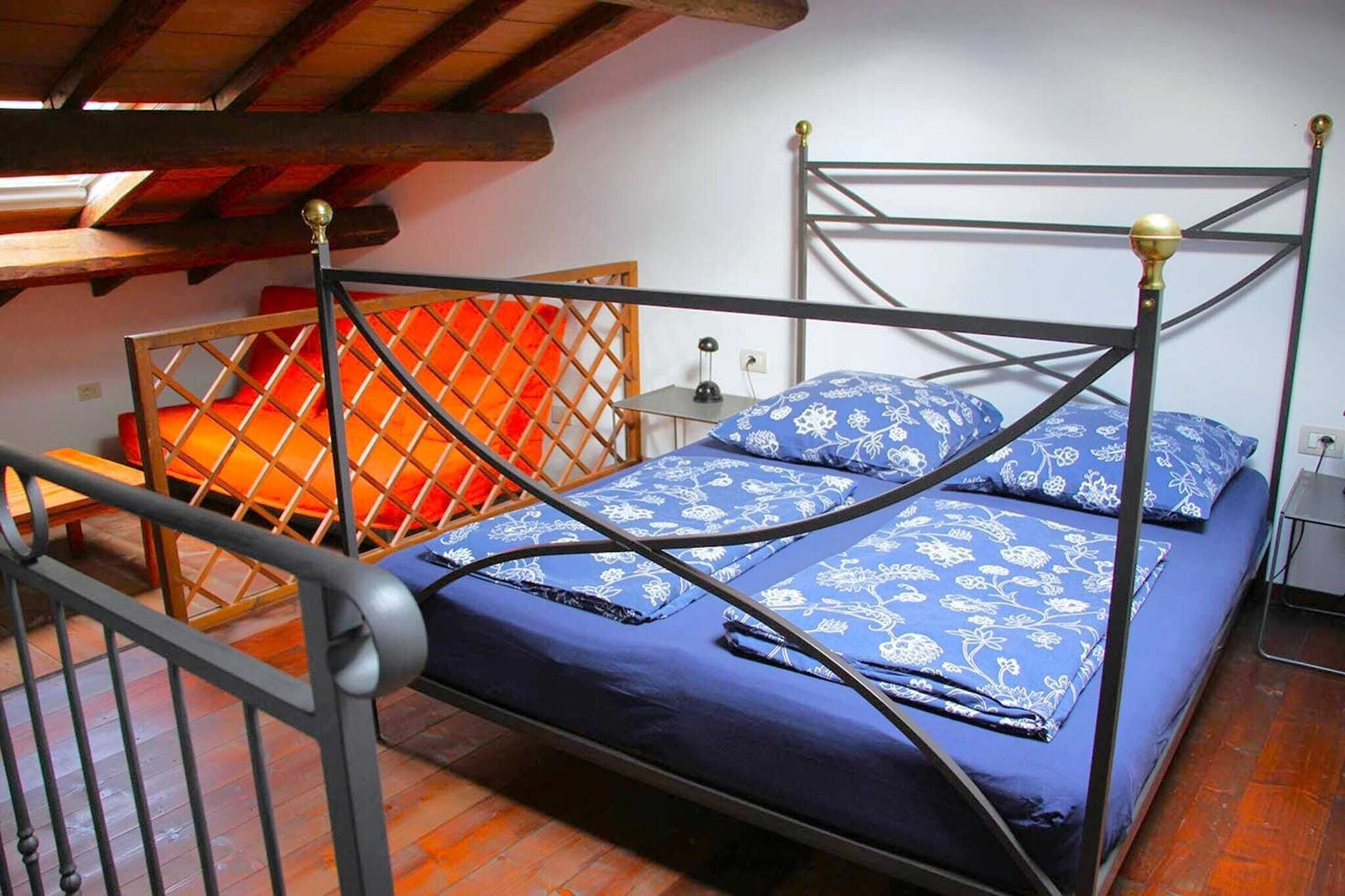 Una cama individual con estructura metálica y colcha azul estampada en una habitación con vigas de madera en el techo.