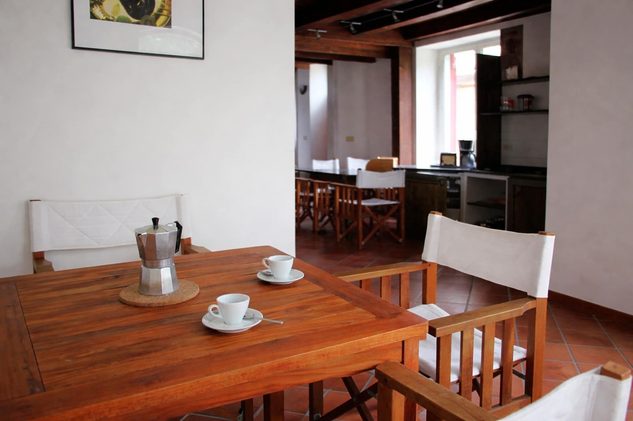 Una mesa de madera con sillas, una cafetera y tazas.