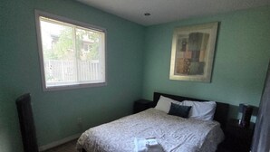 Quarto com cama, janela, pintura e luminária de chão.