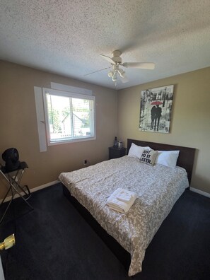 A bedroom with a bed, a ceiling fan, a window, a wall art, and a bedside table.
