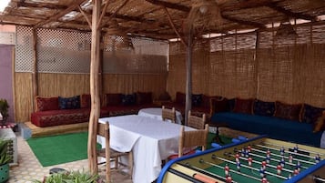 Un espace extérieur abrité, aménagé avec des tables et des chaises, un baby-foot et un canapé.