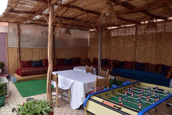 A covered outdoor seating area with tables and chairs, a foosball table, and a sofa. - Lyron Hostel (Marrakech)