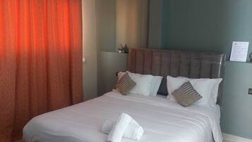 A hotel room with a large bed, a red curtain, and a headboard with multiple pillows.
