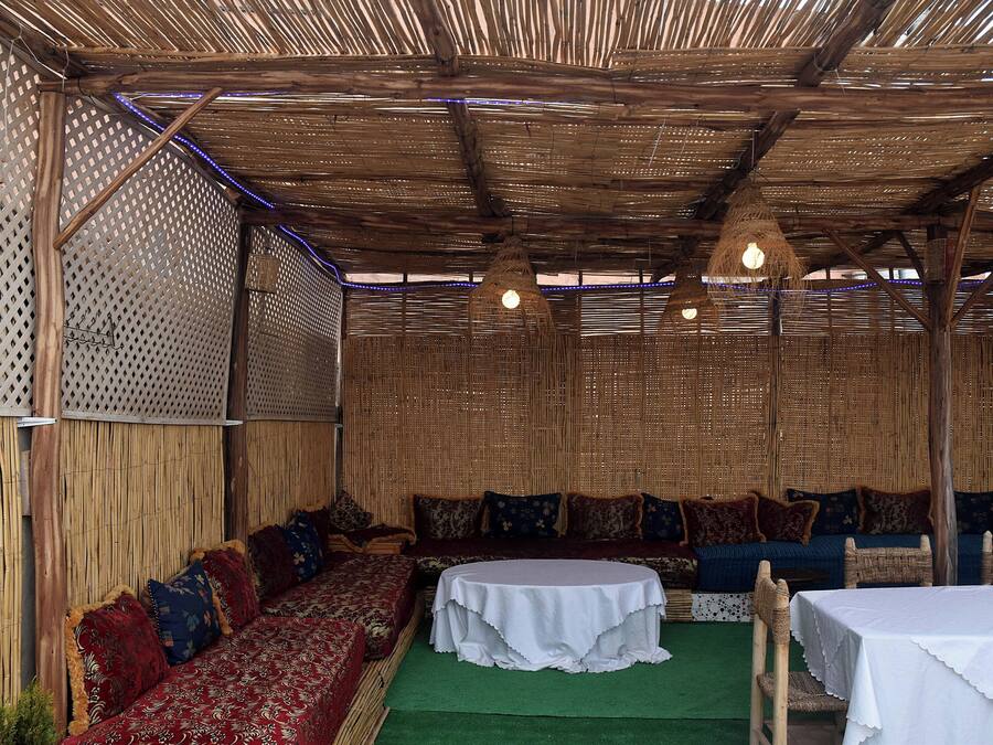 Un área de estar al aire libre con techo de paja, paneles de pared tejidos y una mesa redonda.