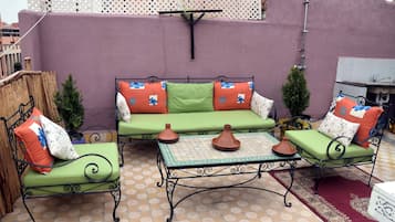 An outdoor seating area with a green sofa and two chairs, a small table with a patterned tablecloth, and a decorative wall.