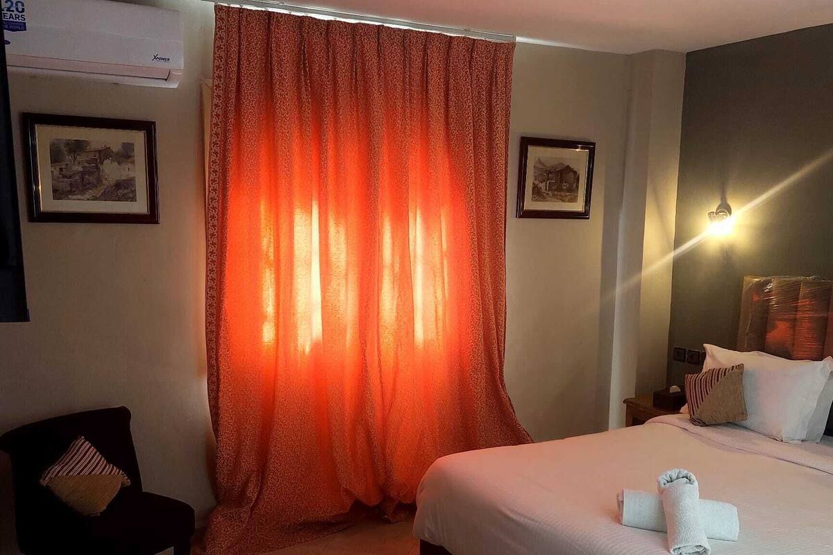 A hotel room with a large bed, a chair, a nightstand, and a wall-mounted lamp.