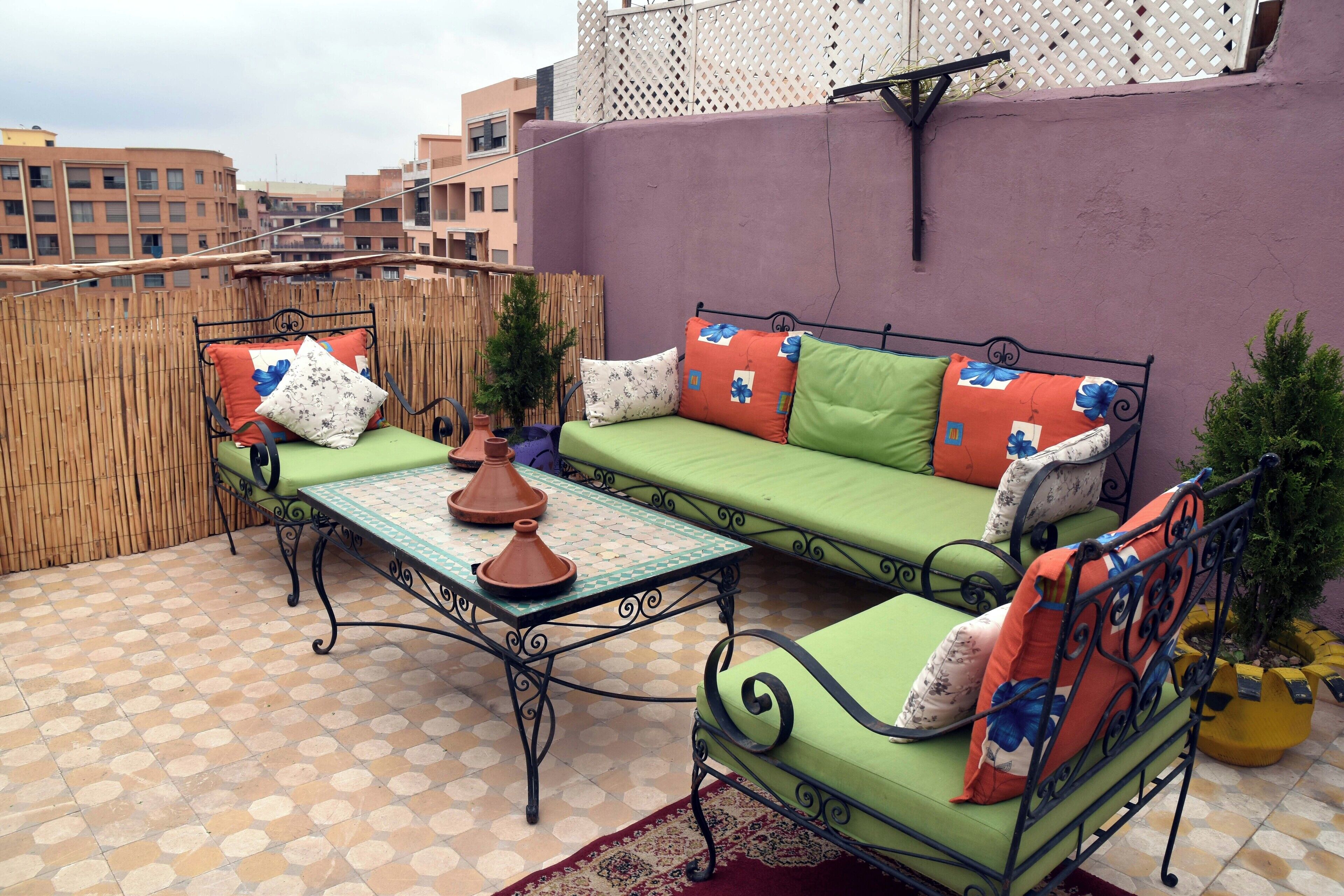 Eine Dachterrasse mit einem grünen Sofa, einem Metalltisch und Terrakottatöpfen.