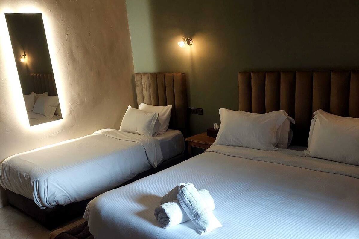 A hotel room with two beds, each with white linens and pillows, a large mirror, and wall-mounted lights.